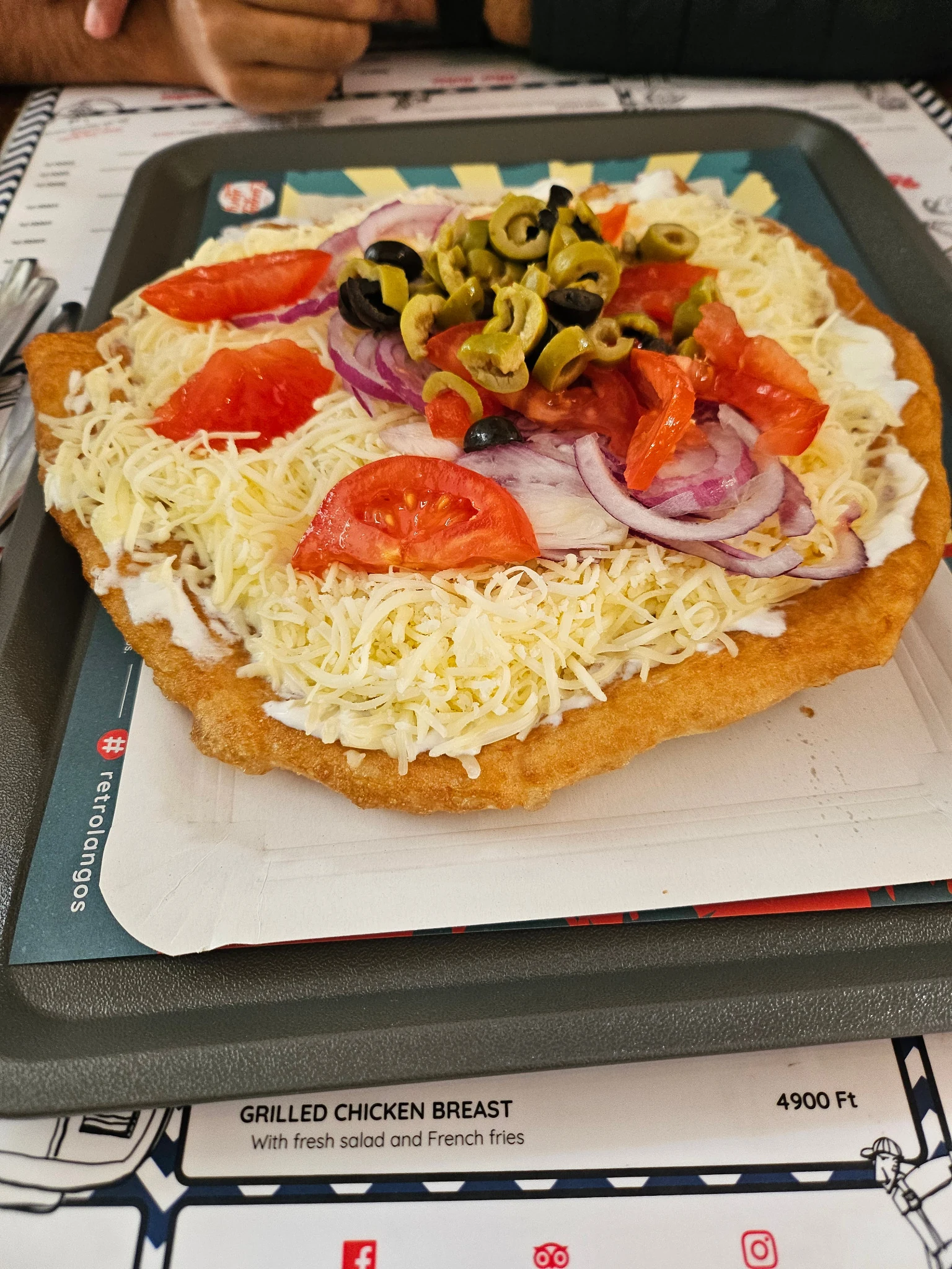 Lángos topped with grated cheese, tomatoes, onion and olives.
