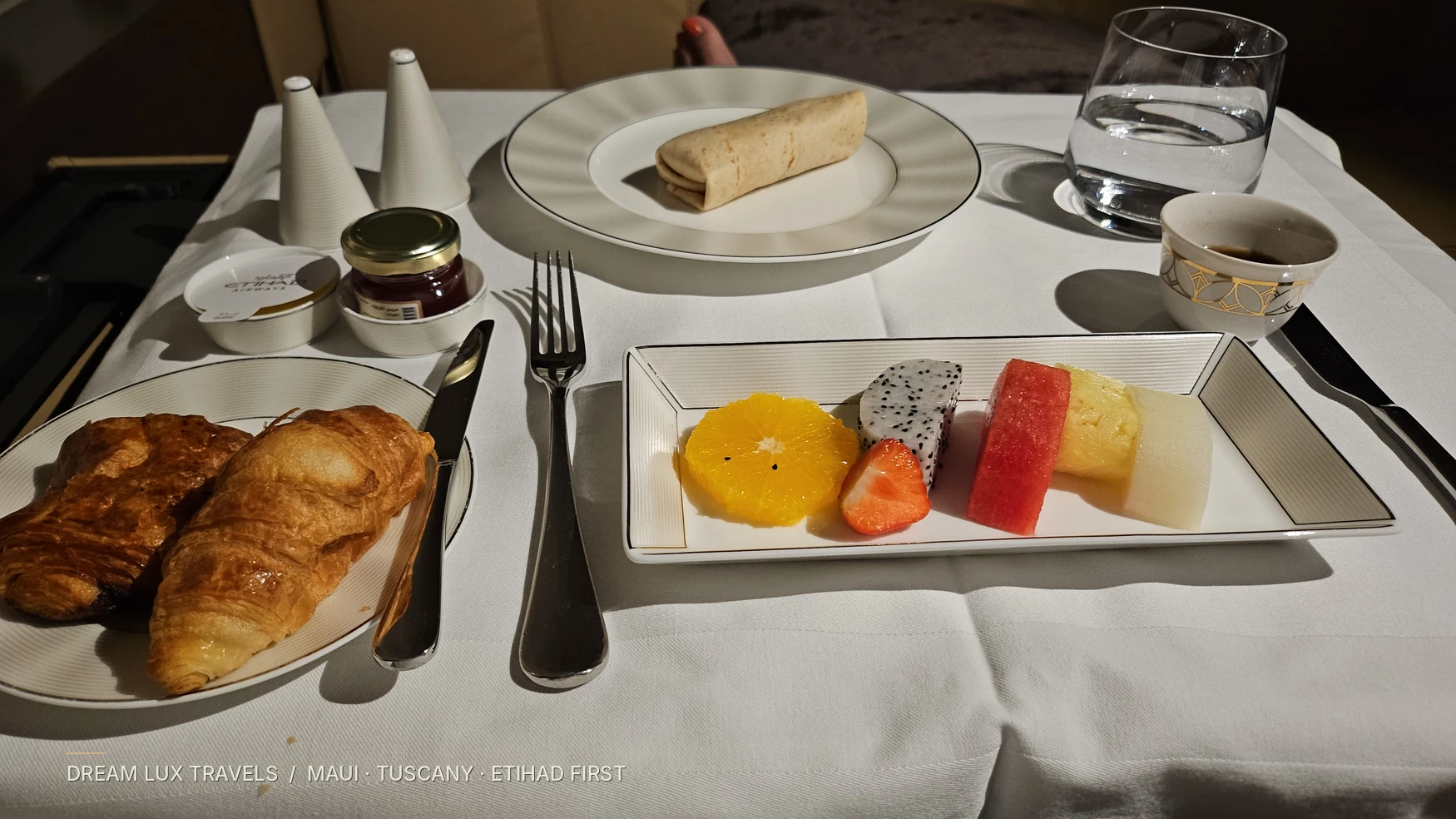 Etihad First Class inflight breakfast served on linen with a fruit plate and croissant.