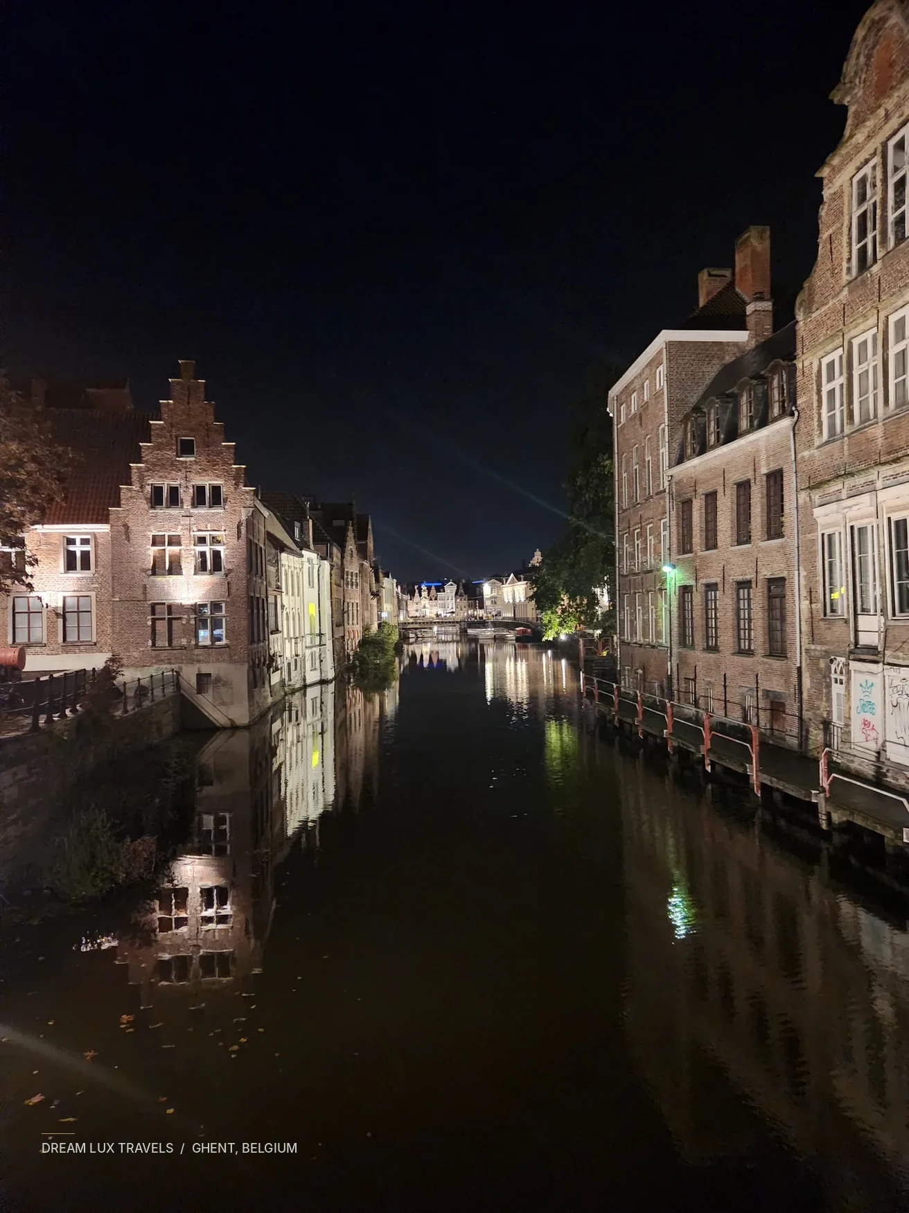 Illuminated historic buildings reflected in a canal in Ghent at night.
