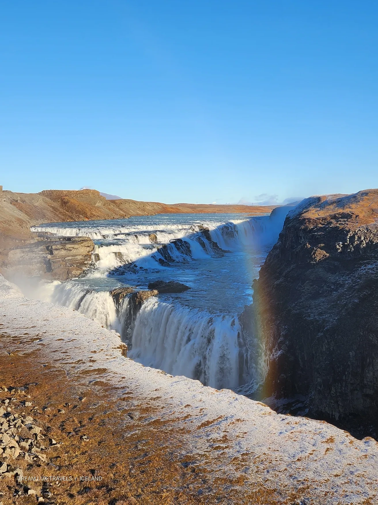 Gullfoss waterfall flowing through a sunlit landscape in Iceland.