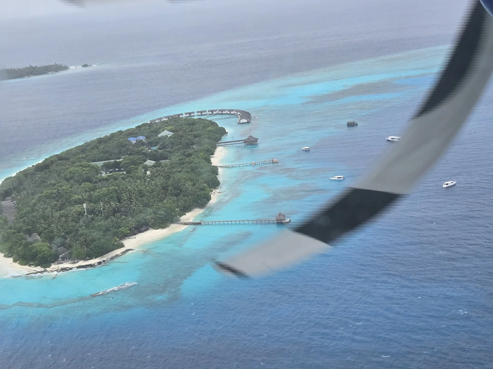 Aerial view of a small Maldivian island bordered by turquoise reef shallows from a seaplane window.