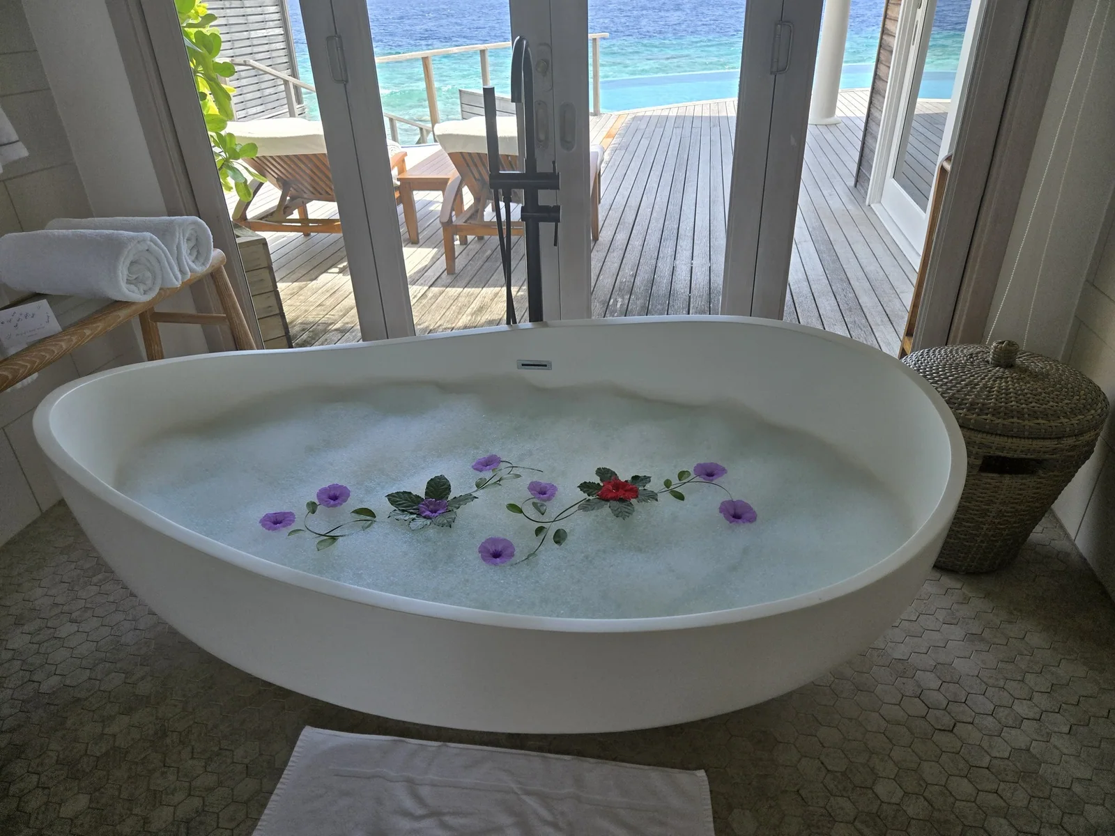 A flower-filled bathtub facing a private deck and sea at Milaidhoo Maldives.