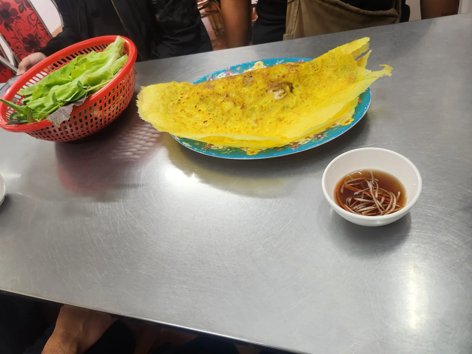 Vietnamese savoury crepe on a blue plate with herbs and dipping sauce during a Saigon food tour.