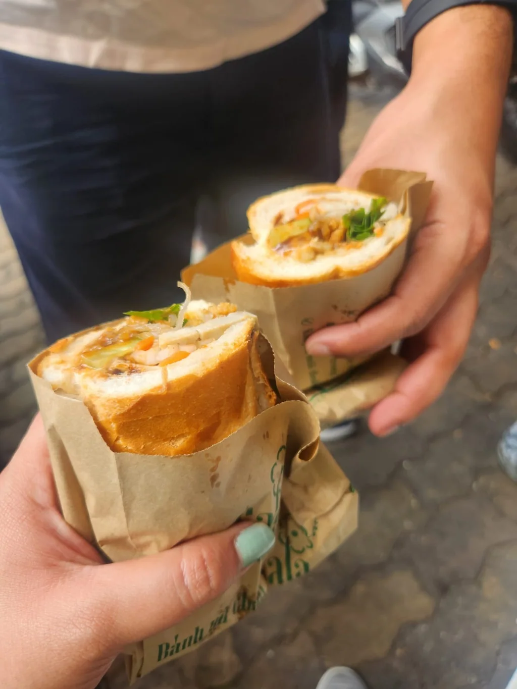 Fresh Vietnamese banh mi sandwiches held in their paper wrappers during the Saigon food tour.