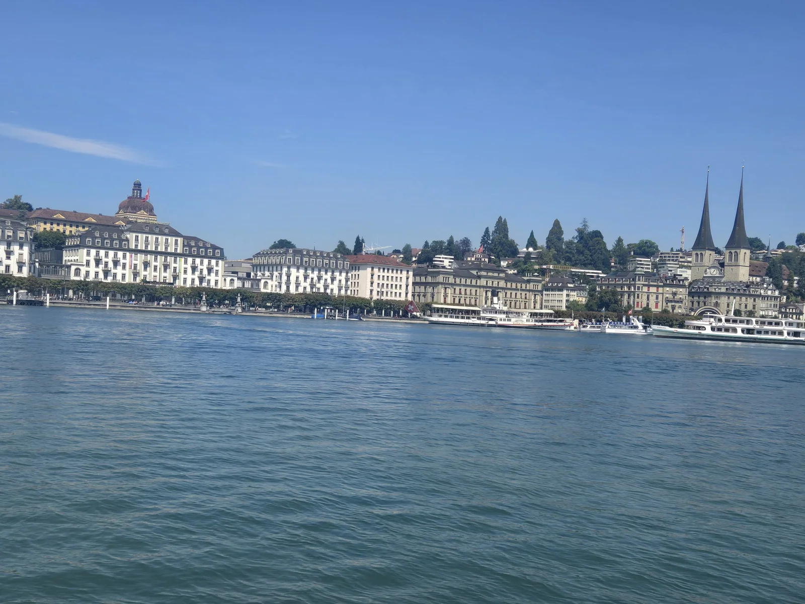 Waterfront buildings and surrounding mountains viewed from Lake Lucerne on a clear day.
